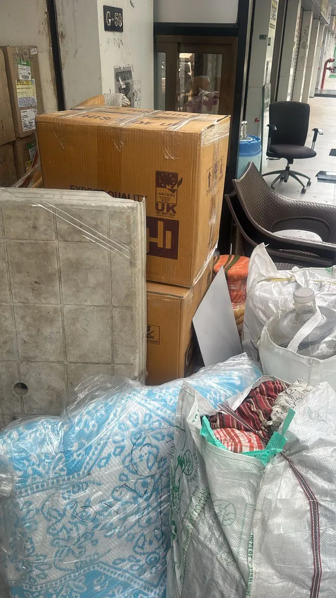 Stacked export-quality cartons, bedding bags and furniture kept at a society entrance during a Surat move